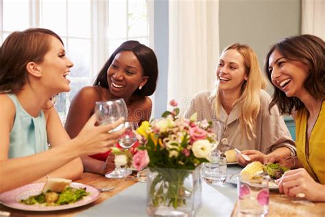 Female Friends At Home Sitting Around Table For Dinner Party Stock
