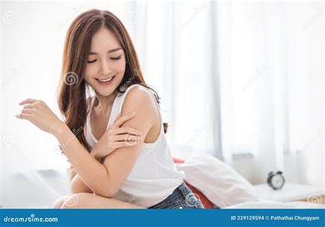 Portrait Of Beauty Smiling Asian Woman Applying A Lotion To Her Arm Skin During Her Morning