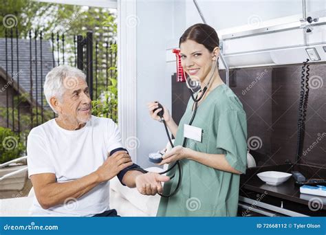 Confident Nurse Examining Blood Pressure Of Senior Man Stock Photo