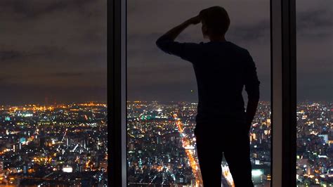 Man Looking Out Large Windows High Above A Sprawling City Stock Video