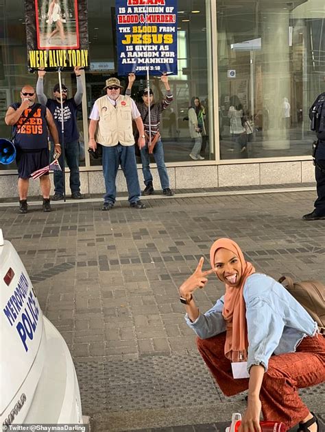 Smiling Woman In Hijab Flashing Peace Sign In Front Of Anti Muslim
