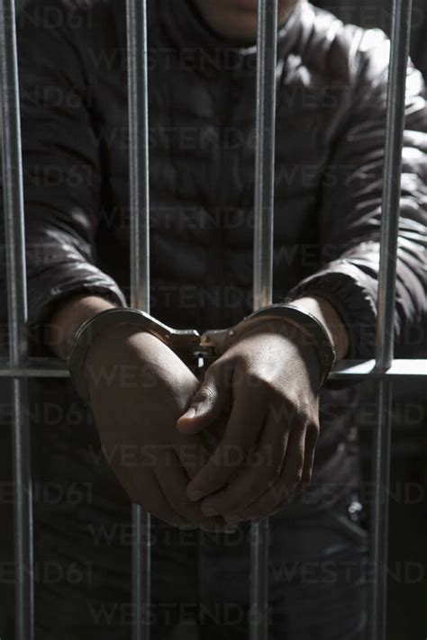 A Prisoner Behind Bars With Hands Cuffed Stock Photo
