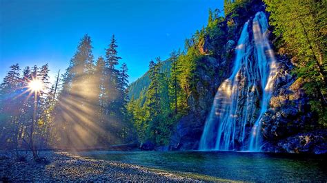 Waterfalls From Rock Pouring On Lake Between Green Trees Covered Mountains Under Blue Sky Hd