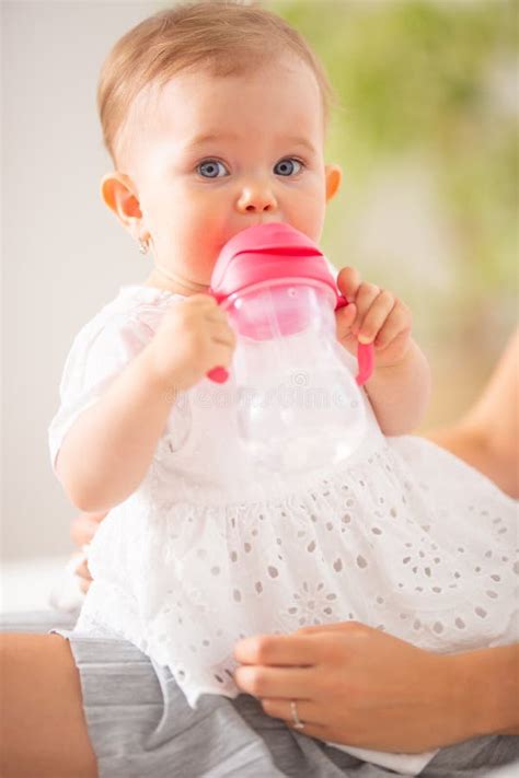 Baby Girl Holds An Empty Milk Bottle With Both Of Her Hands Holding It Close To Her Mouth Stock