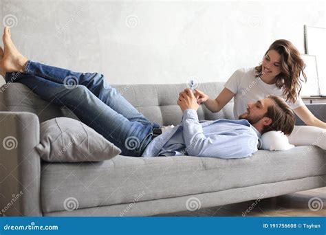 Young Loving Couple Relaxing On Sofa Together Husband Lying On Wife Legs Resting On Couch Stock