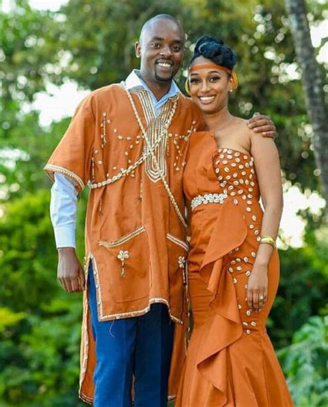 a man and woman dressed in traditional african clothing posing for a photo together with trees