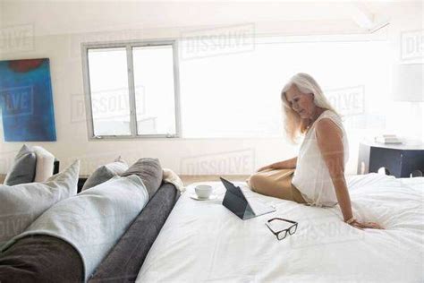 Senior Woman Sitting On Bed And Looking At Tablet Computer Stock