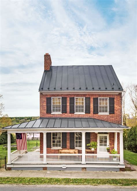 A Red Brick House With Black Shutters And An American Flag On The Porch