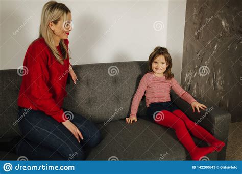 Blond Hair Mom In Red Sweater Sitting On Sofa With Her Daughter