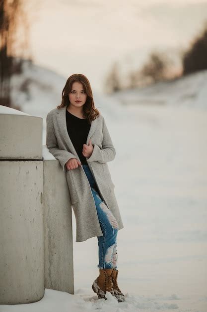 Free Photo Vertical Shot Of A Sexy Woman With A Grey Jacket Leaning On The Wall On A Snowy Park