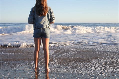 girl standing in the surf looking out at the water by stocksy contributor carolyn lagattuta