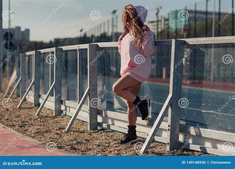 Young Happy Attractive Woman Posing On A Fence Near A Running Track