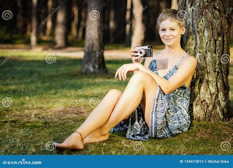 Beautiful Woman Sitting With A Camera Near A Tree In The Forest Stock