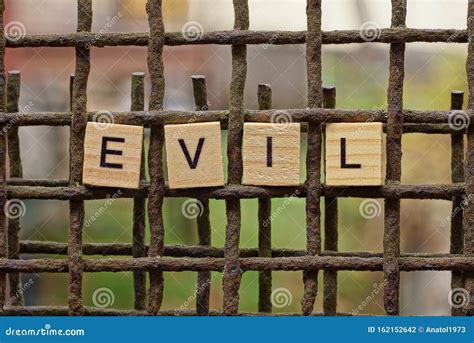 The Word Evil From Wooden Letters On The Rusty Iron Bars Stock Photo