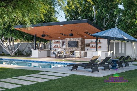 An Outdoor Kitchen Next To A Pool With Lounge Chairs And Umbrellas On