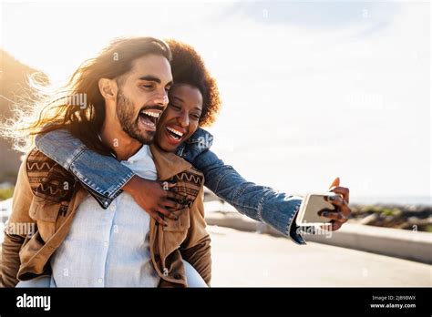 Happy Multiracial Couple Having Fun Taking Selfie With Mobile Smartphone During Vacations