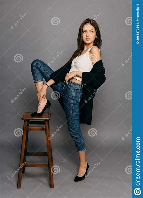 Brunette With Long Hair In Jacket And Jeans Put Her Foot On The Back Of