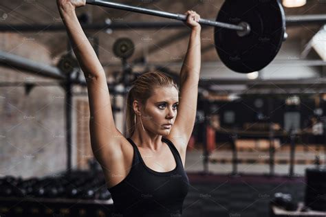 Young Woman Lifting Weights Over Her Head In A Gym High Quality