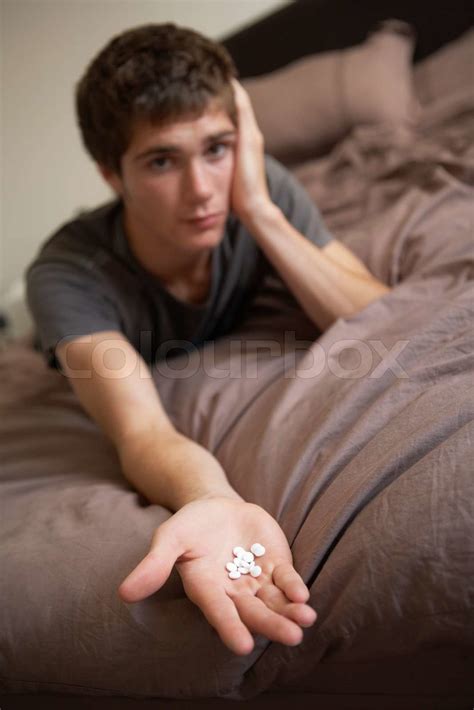 Depressed Teenage Boy Sitting In Bedroom With Pills Stock Image