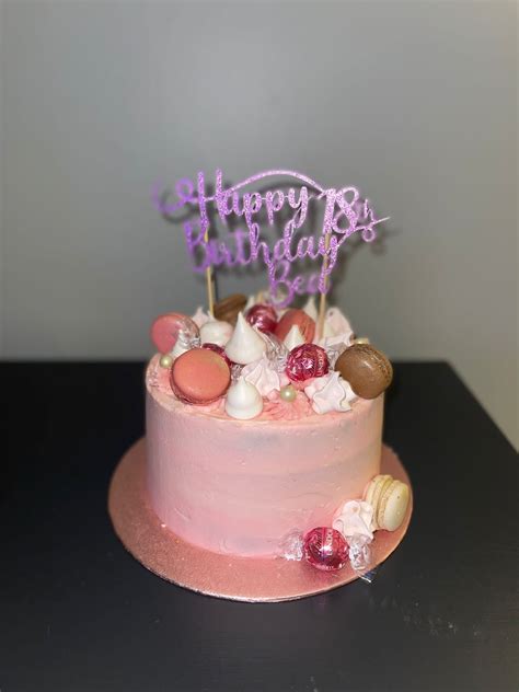 vanilla sponge covered in pink buttercream and topped with macarons meringue kisses and lindt