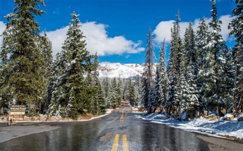 Road Between Snow Covered Trees And Mountains Under White Clouds Blue