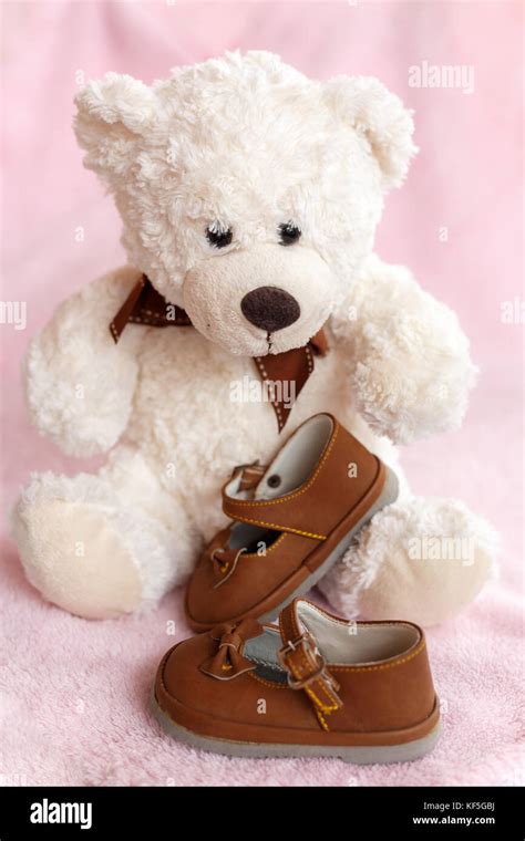 Teddy Bear With Pair Of Mary Jane Style Baby Shoes Against A Pale Pink