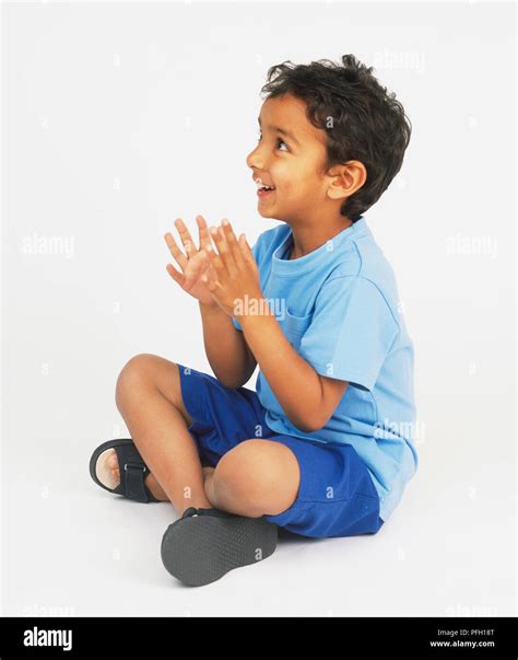 Boy Sitting Cross Legged On Floor Looking Up And Clapping Hands Stock