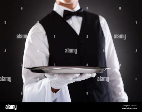 Portrait Of A Male Waiter Holding Tray Over Black Background Stock