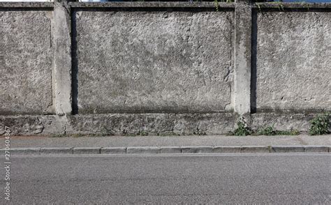 A Rough Concrete Wall With A Gray Sidewalk And An Asphalt Road Urban
