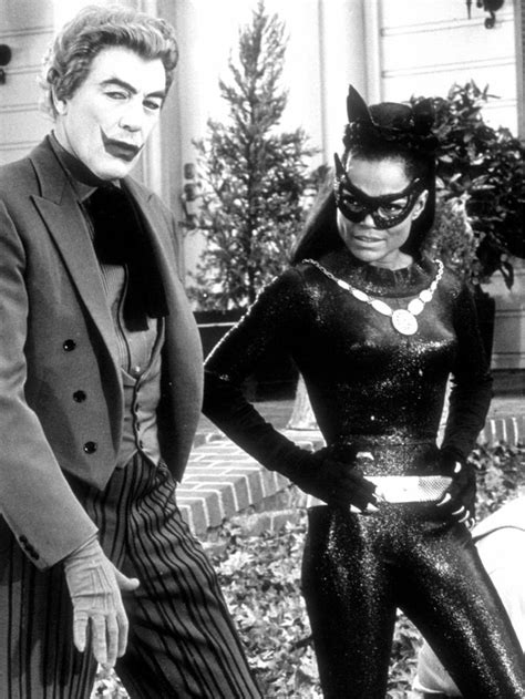 Two People Dressed Up As Batman And Catwoman Standing Next To Each Other In Front Of A House