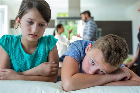 Sad Kids Leaning On Sofa While Parents Arguing In Background Stock