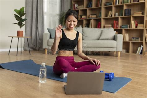 Online Domestic Training Happy Young Asian Lady Waving To Webcam Sitting On Yoga Mat In Front