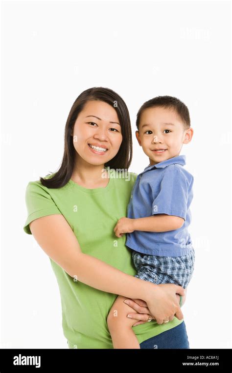 Asian Mother Holding Son On Hip Smiling In Front Of White Background