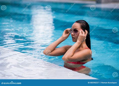Woman Wearing Red Swimsuit And Sunglasses Sitting In Swimming Pool