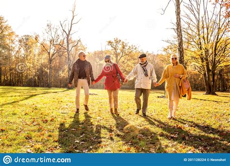 Senior Friends Walking Together In Beautiful Sunny Autumn Park Holding