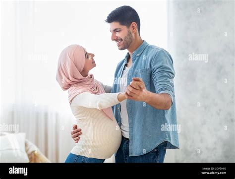 Romantic Arab Pregnant Couple Dancing Waltz At Home In Living Room Interior Happy Muslim Man