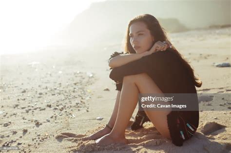 Thoughtful Woman Hugging Knees While Sitting At Beach During Sunny Day