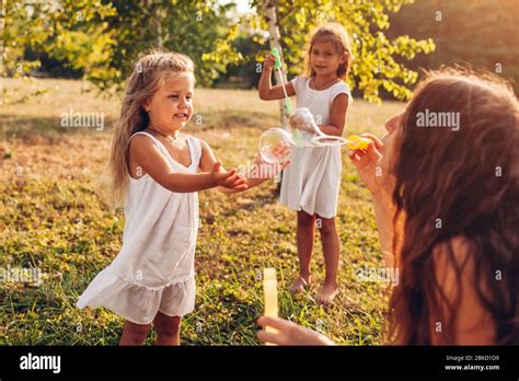Mother Helps Daughters To Blow Bubbles In Summer Park Kids Having Fun