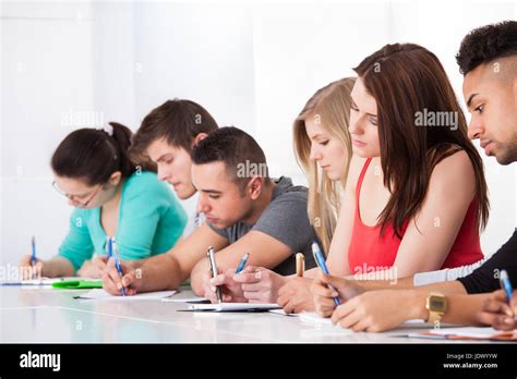 Row Of Multiethnic College Students Writing At Desk In Classroom Stock