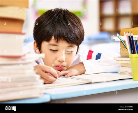 Tired And Bored Asian Elementary School Boy Doing Homework In Stock