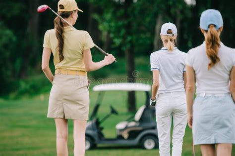 Back View Of Women With Golf Gear Walking On Green Lawn Stock Photo