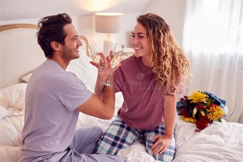 Loving Couple Wearing Pyjamas In Bed At Home Celebrating Birthday Or Anniversary With Champagne
