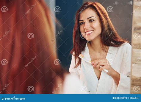 Beautiful Young Woman Standing In Bathroom Near The Mirror And Brushing Her Teeth Stock Image