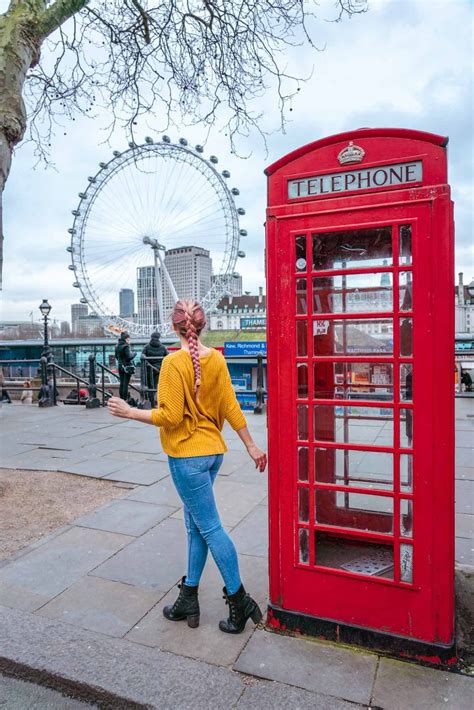 A Woman Standing Next To A Red Phone Booth In Front Of The London Eye