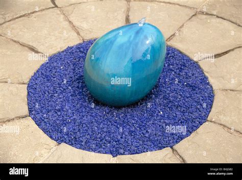 Close Up Of Blue Ceramic Egg Shaped Water Feature On Circular Bed Of