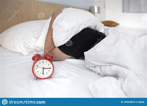 Young Male Stressed By His Alarm Clock While Sleeping On His Bed With