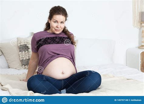 Portrait Of Joyful And Smiling Pregnant Woman With Naked Belly Sitting