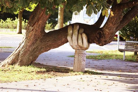 Sculpture Of A Large Hand Holding Up A Large Tree Limb Person