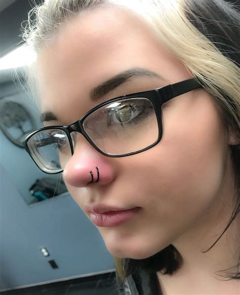 A Woman With Glasses And Nose Piercings On Her Nose Is Looking At The Camera