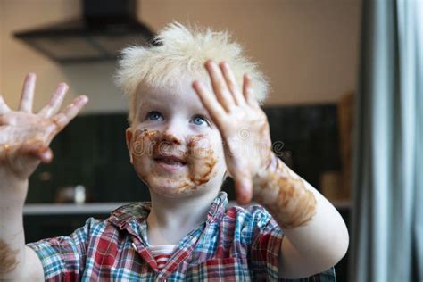 A Young Boy With Hands And Face Covered In Chocolate After Helping In